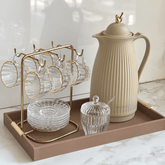 Garrafa térmica bege 1 litro com detalhes dourados, acompanhada de xícaras de vidro com suporte, açucareiro e pires sobre bandeja. Ideal para compor mesa posta com xícaras de café, bandeja elegante e acessórios para servir com estilo.
